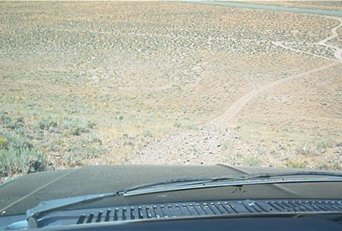 1986 Ford Bronco - View from inside a vehicle as it navigates a dirt path through a dry, brush-covered landscape.
