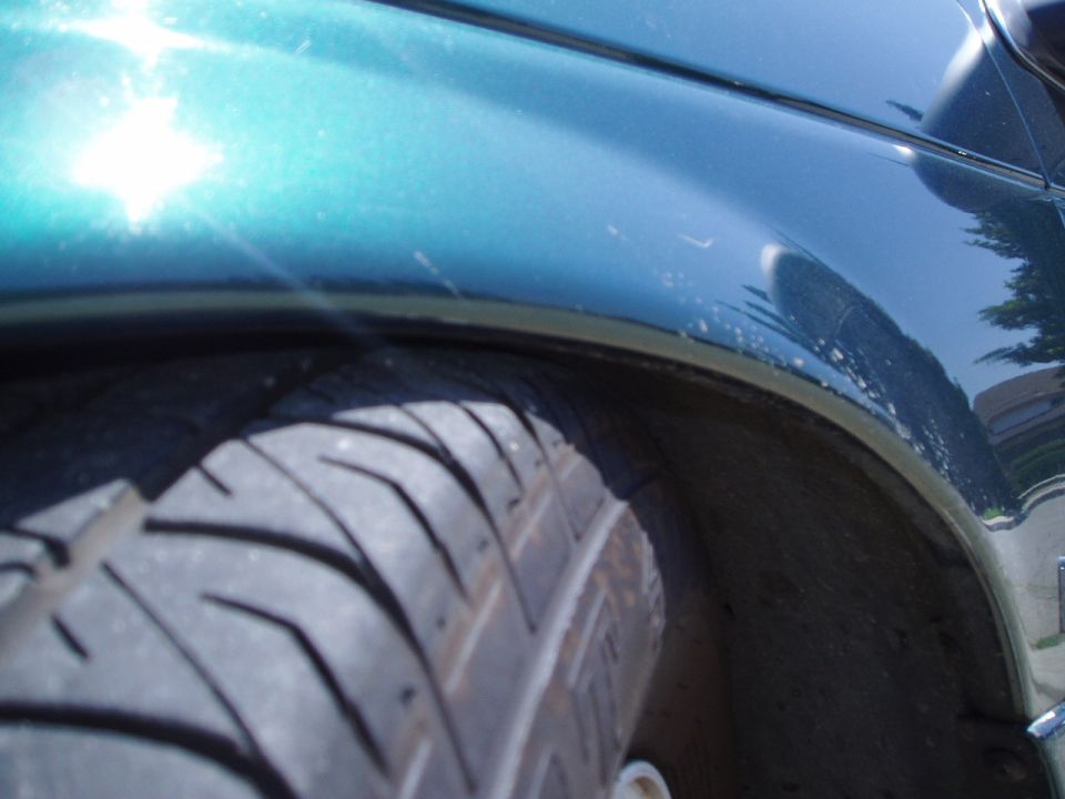 Close-up of a teal car's fender and tire. The paint has some scuffs