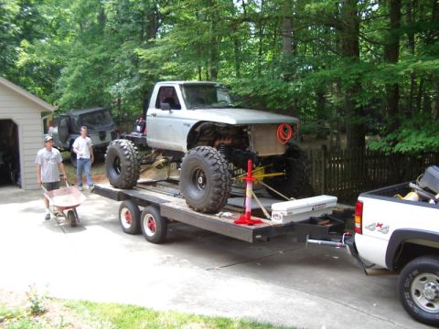 1985 Ford Bronco - Modified pickup truck with oversized tires is loaded onto a trailer for transport.