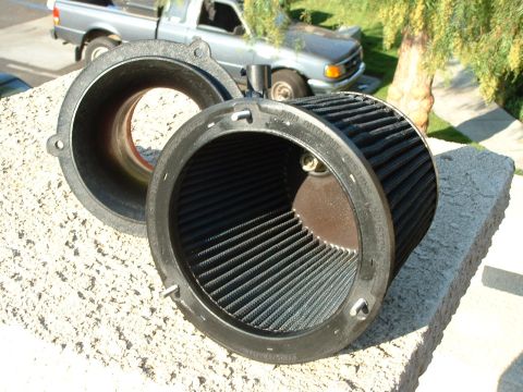 1992 Ford Crown Victoria - An engine air filter and its housing sit on a textured surface, with a pickup truck visible behind them.