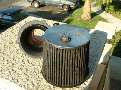 1992 Ford Crown Victoria - An aftermarket air filter sits on a textured surface, with a pickup truck and sedan visible in the background.