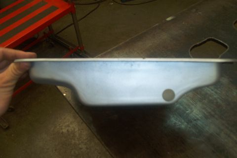 1983 Ford Bronco - A metal oil pan is shown from the side, with a circular drain plug opening visible.