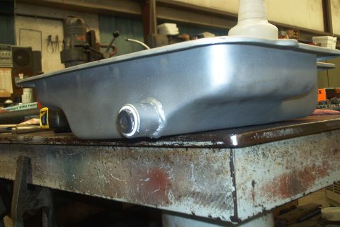 1983 Ford Bronco - A metal oil pan sits on a workbench in a workshop, with various tools and equipment visible in the background.