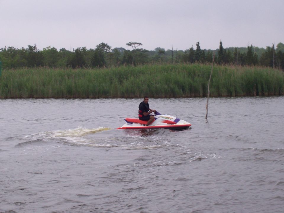 Man riding red and white Yamaha jet ski across water near marsh grass