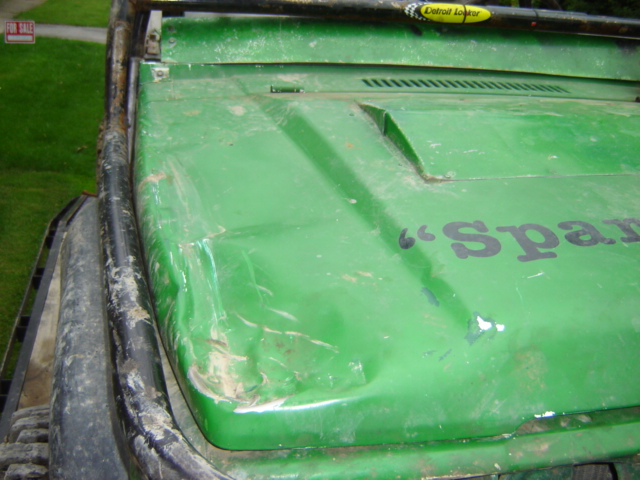 Green off-road vehicle hood with dents and scratches, "Spar" text visible