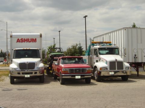 1992 Ford Bronco - A red 1992 Ford F-150 pickup is parked between two tow trucks and a trailer.