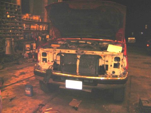 1992 Ford Bronco - Front end of a red pickup truck with the hood up and the grille and radiator removed, parked in a workshop.