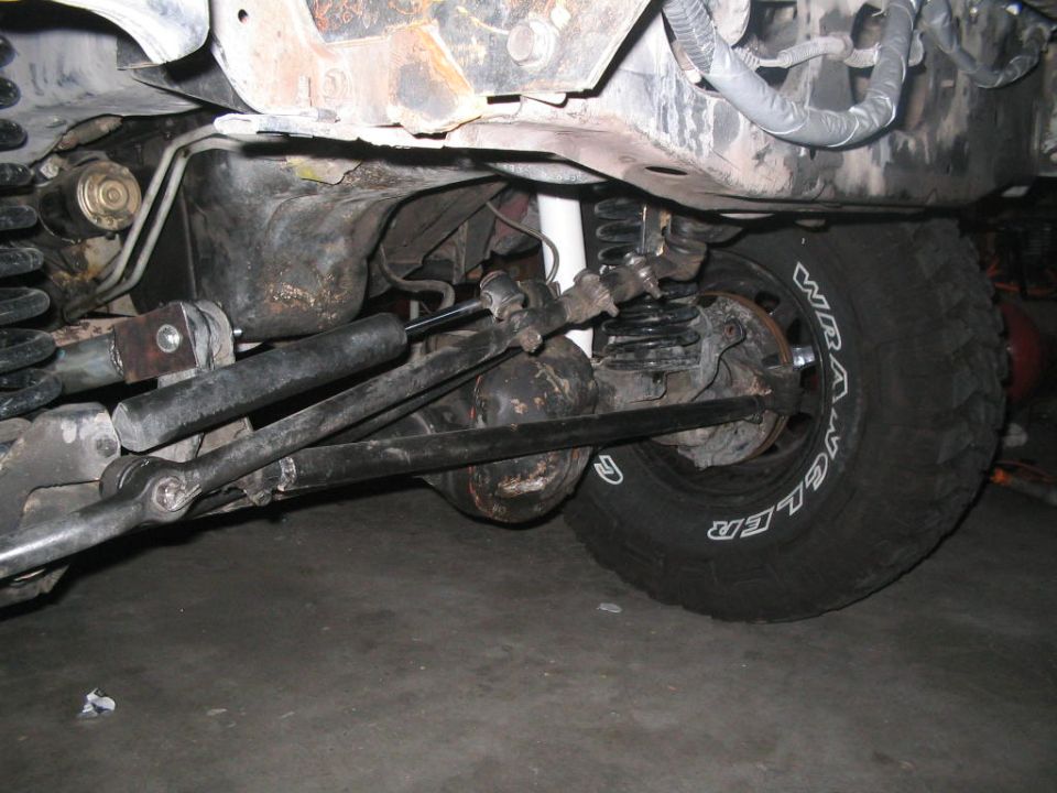 Undercarriage of a vehicle showing suspension, steering linkage, and a tire with "WRANGLER" text