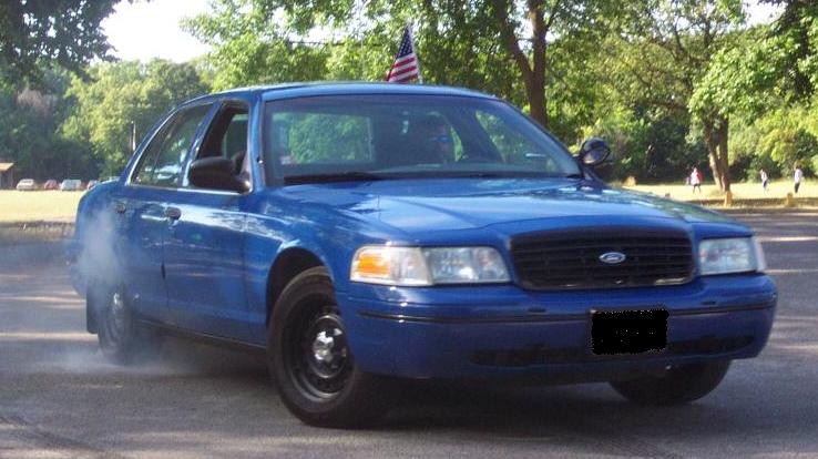 Blue Ford Crown Victoria sedan doing a smoky burnout in a park lot