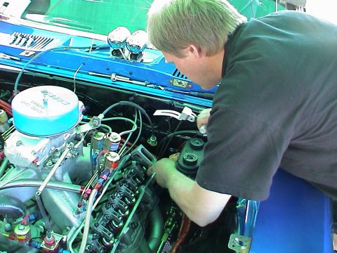 1979 Ford Bronco - A mechanic works on the engine of a blue vehicle, with the Supermotors.net logo in the corner.