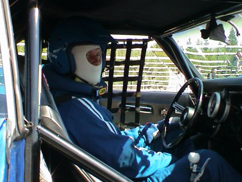 1979 Ford Bronco - Driver wearing a helmet and face covering sits in the interior of a race car, ready for the track.