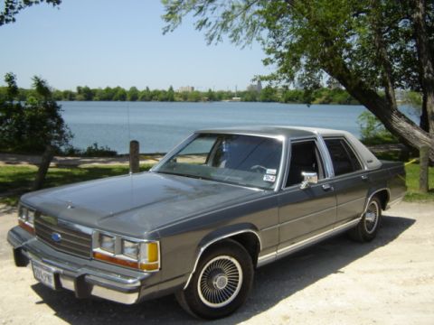 1988 Ford LTD Crown Victoria - This 1988 Ford Crown Victoria LTD is parked near a body of water with trees and a city skyline in the background.