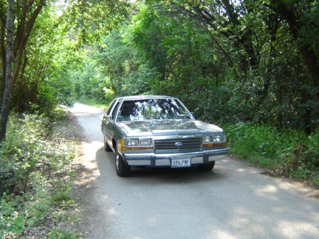 1988 Ford Crown Victoria LTD driving on a dirt road surrounded by trees