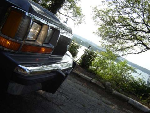 1988 Ford LTD Crown Victoria - The front of a 1988 Ford Crown Victoria LTD is shown with a body of water and trees in the background.