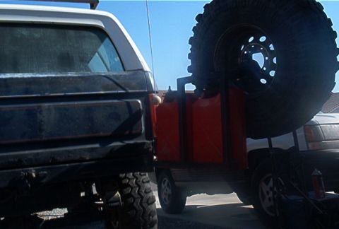 1986 Ford Bronco - A spare tire and multiple jerry cans are mounted on the rear of a vehicle, seen next to a Ford Bronco.