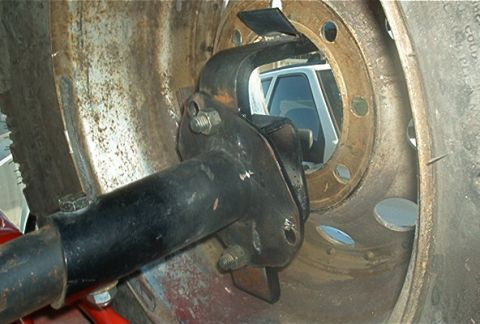 1986 Ford Bronco - A white SUV is partially visible through the holes of a rusty tire rim and suspension assembly.