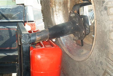 1986 Ford Bronco - A red jerry can is attached to the vehicle's frame, positioned near the large tire and suspension components.