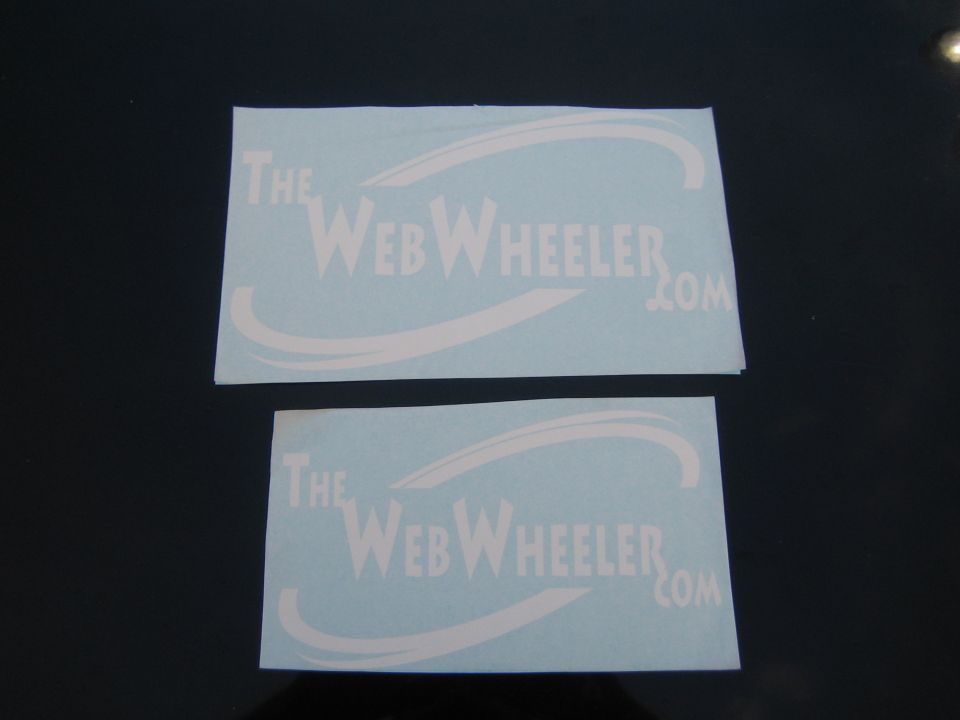 Two TheWebWheeler.com vinyl decals on a dark surface