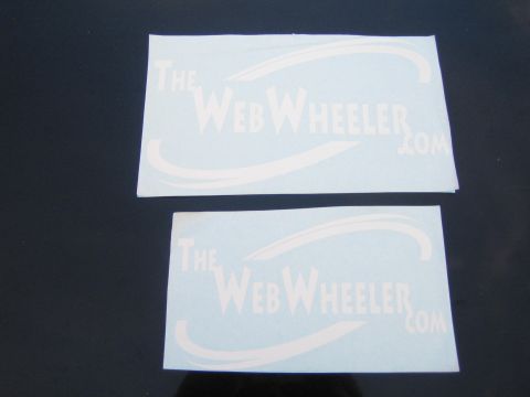 1990 Ford Bronco - Two light-blue vinyl stickers reading 'TheWebWheeler.com' are arranged on a dark surface.