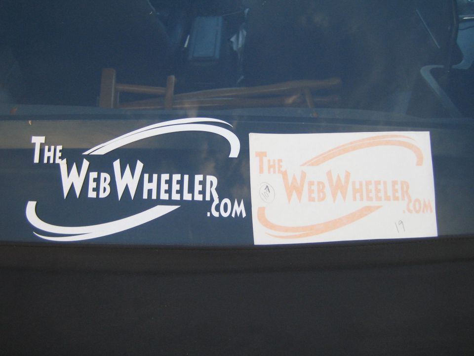 White and orange 'TheWebWheeler.com' decals side by side on a vehicle window