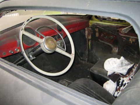1968 Ford Mustang - Interior of a car with a white steering wheel and red dashboard. The car appears to be in a state of disrepair.