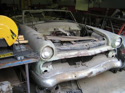 1968 Ford Mustang - A vintage car is undergoing restoration in a workshop, with its front end partially dismantled and the engine exposed.