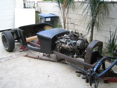 1968 Ford Mustang - A disassembled car chassis with its engine exposed sits on jack stands in a driveway.