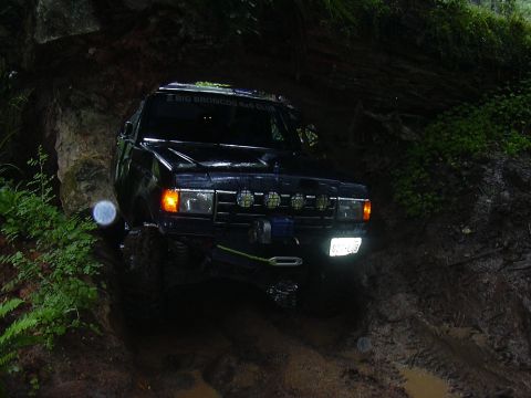 1991 Ford Bronco - A black SUV navigates a muddy off-road trail with dense foliage on either side.