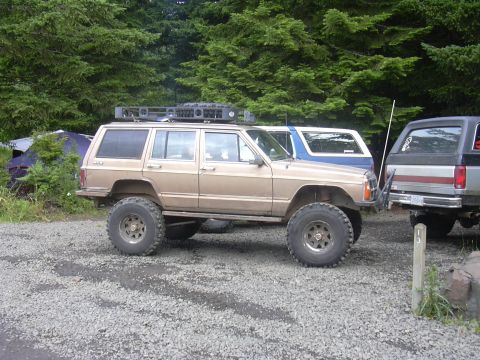 1991 Ford Bronco - Modified Jeep Cherokee XJ and other vehicles parked outdoors near trees and tents.