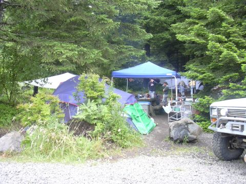 1991 Ford Bronco - A campsite is set up in a wooded area with tents and a canopy, and a vehicle is parked nearby.