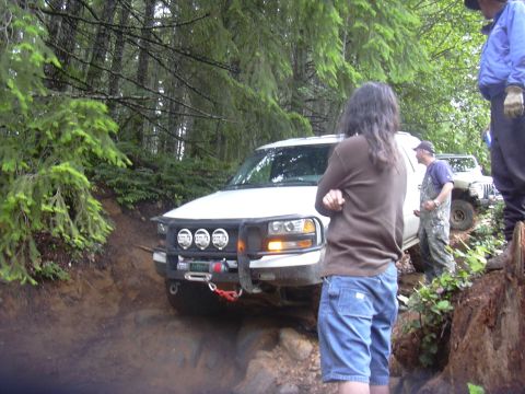 1991 Ford Bronco - A white SUV navigates a challenging off-road trail with another vehicle visible behind it.