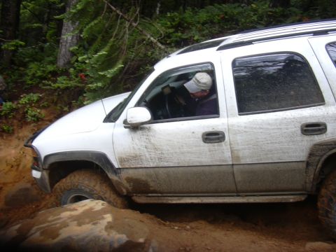 1991 Ford Bronco - A white SUV is shown off-roading on a muddy, rocky trail.