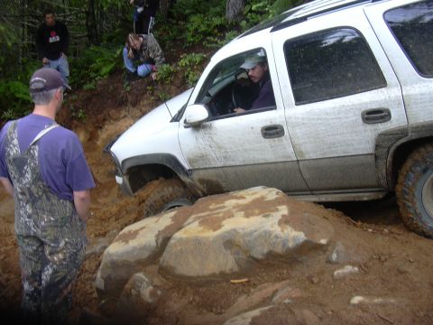 1991 Ford Bronco - White SUV stuck on a challenging off-road trail with onlookers.