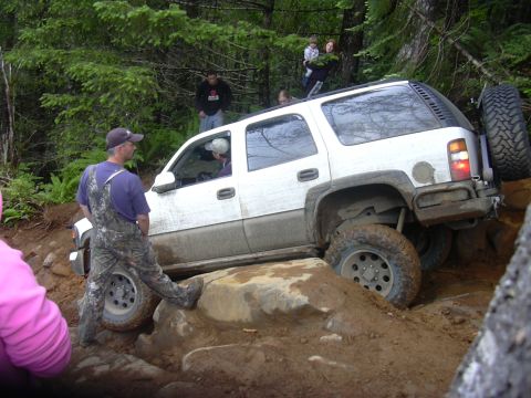 1991 Ford Bronco - A white SUV is shown attempting to traverse a difficult off-road path with large rocks and mud.
