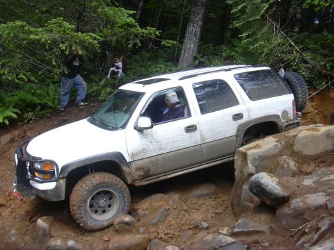 1991 Ford Bronco - A white SUV navigates a challenging off-road trail with steep inclines and large rocks.