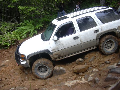 1991 Ford Bronco - White SUV tackling a challenging off-road trail with mud and rocks.