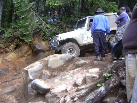 1991 Ford Bronco - A group of people observe an off-road vehicle as it maneuvers through a challenging, natural obstacle course.