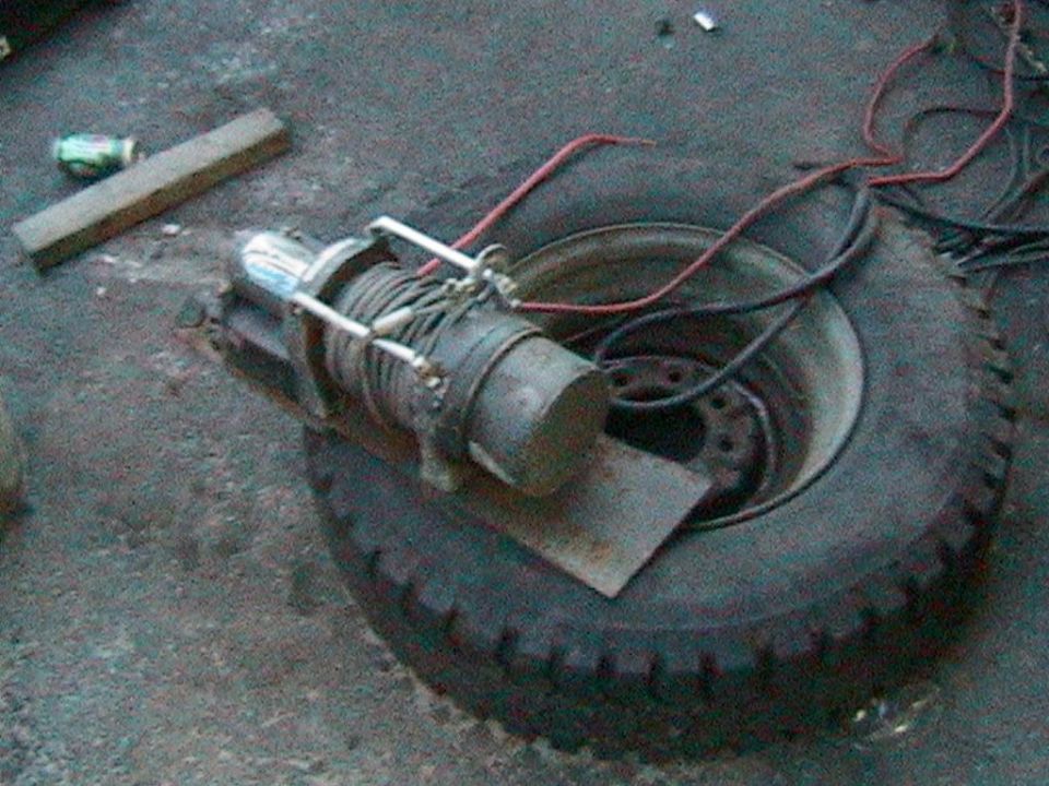 Electric winch with spooled steel cable sitting on a tire and wheel on a shop floor