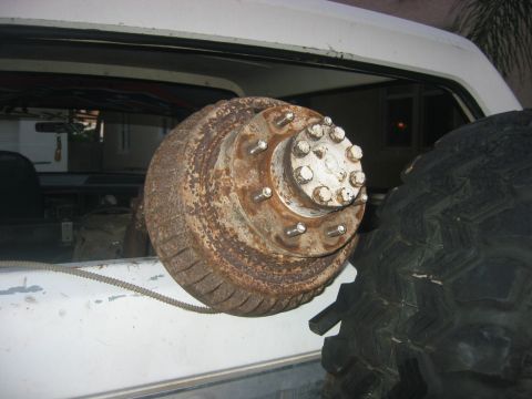 1989 Ford Bronco - A rusty brake drum and hub assembly is visible inside a vehicle, next to a large tire.