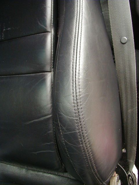 1994 Ford Probe - The interior of a car shows a black leather seat with a seatbelt, a watermark from Supermotors.net.