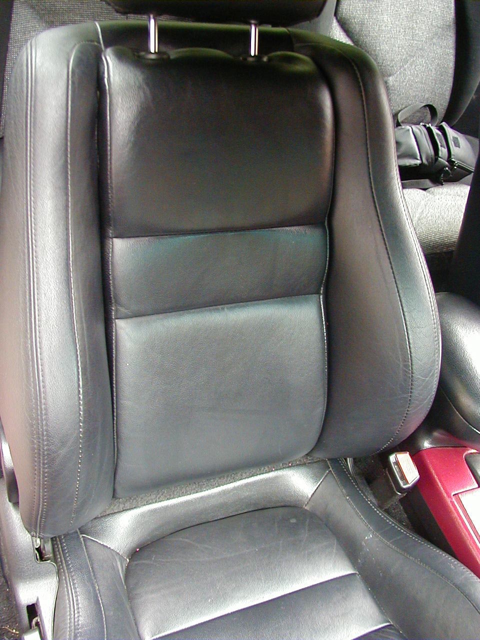 black leather car seat with red trim visible on the right