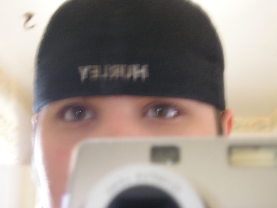 person wearing a black Hurley hat takes a selfie with a digital camera