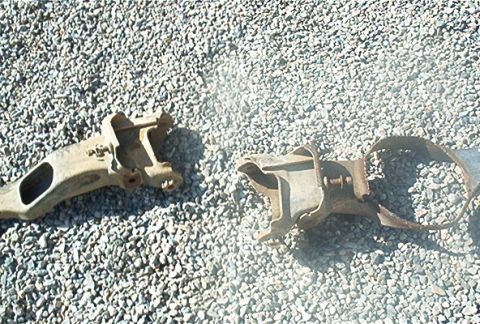 1986 Ford Bronco - Two rusty metal vehicle suspension components lie on a bed of gravel.