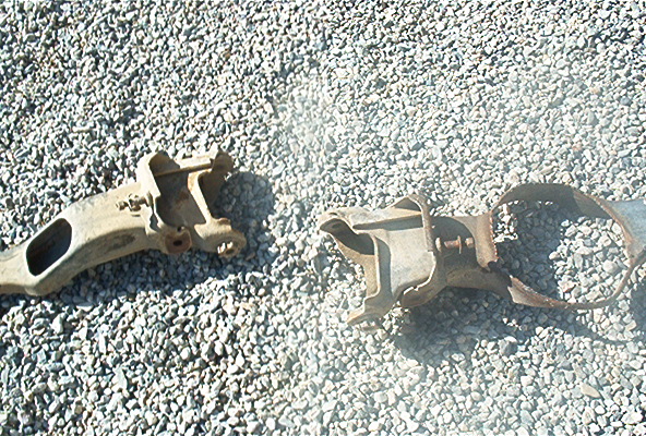 Two rusty metal vehicle suspension parts on gravel
