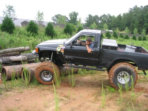 1986 Ford F-150 - A driver maneuvers a modified black pickup truck over an obstacle course made of logs and pipes.