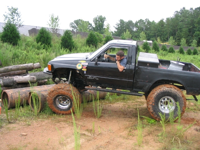 Black pickup truck with lifted suspension and large tires navigating a course of logs and pipes
