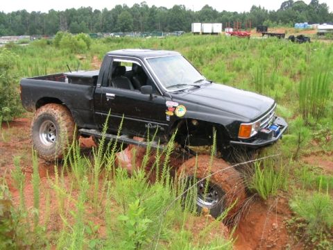 1986 Ford F-150 - This black pickup truck is equipped with large off-road tires and is shown navigating a challenging muddy course.