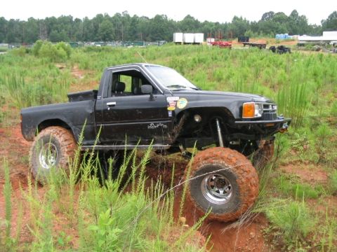 1986 Ford F-150 - Modified Toyota pickup truck with oversized tires on a dirt trail.