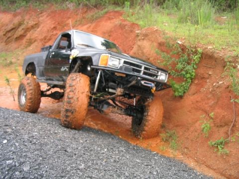 1986 Ford F-150 - Modified black Toyota pickup truck navigates a muddy off-road course.