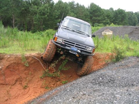 1986 Ford F-150 - This modified Toyota pickup truck tackles a challenging off-road obstacle with its large tires and lifted suspension.